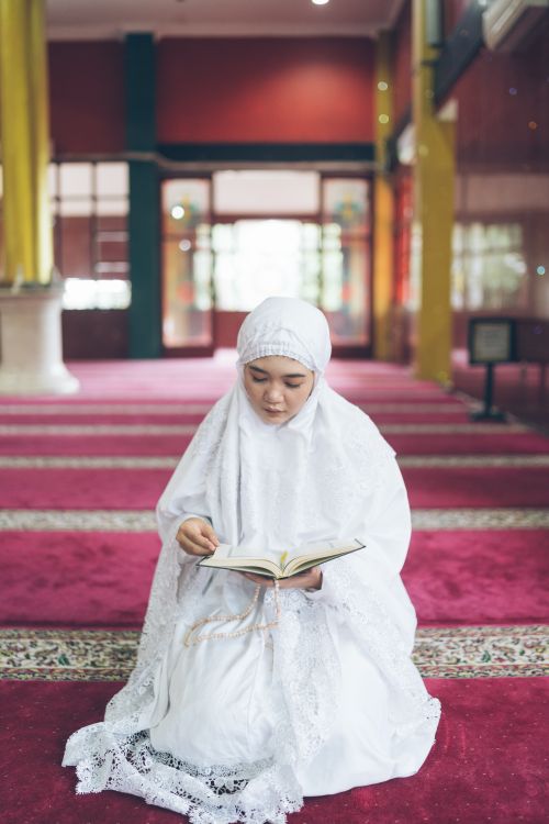 Wanita berhijab membaca Al-Quran di masjid